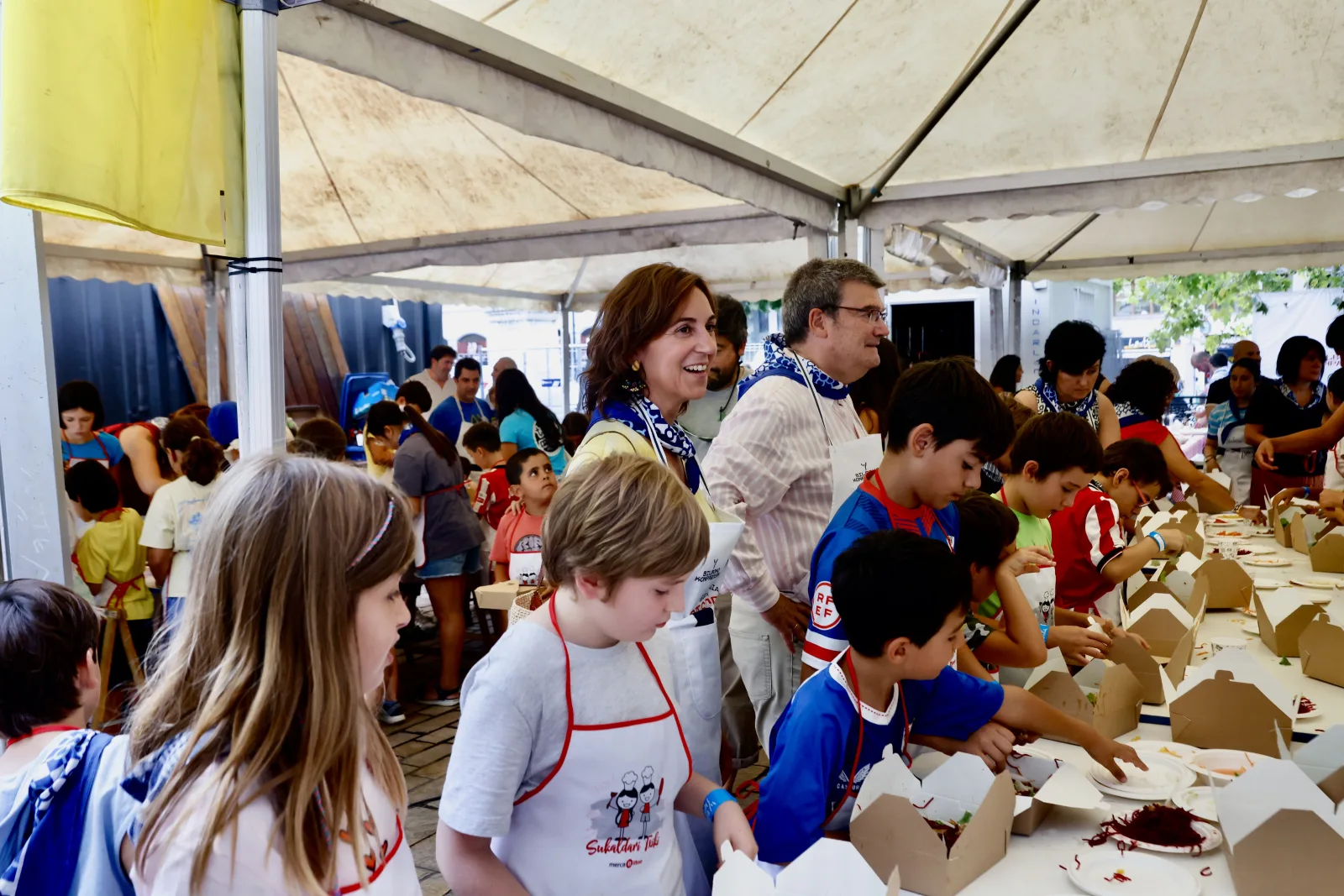Vista general de la carpa del taller, con niños en la mesa y personas adultas detrás