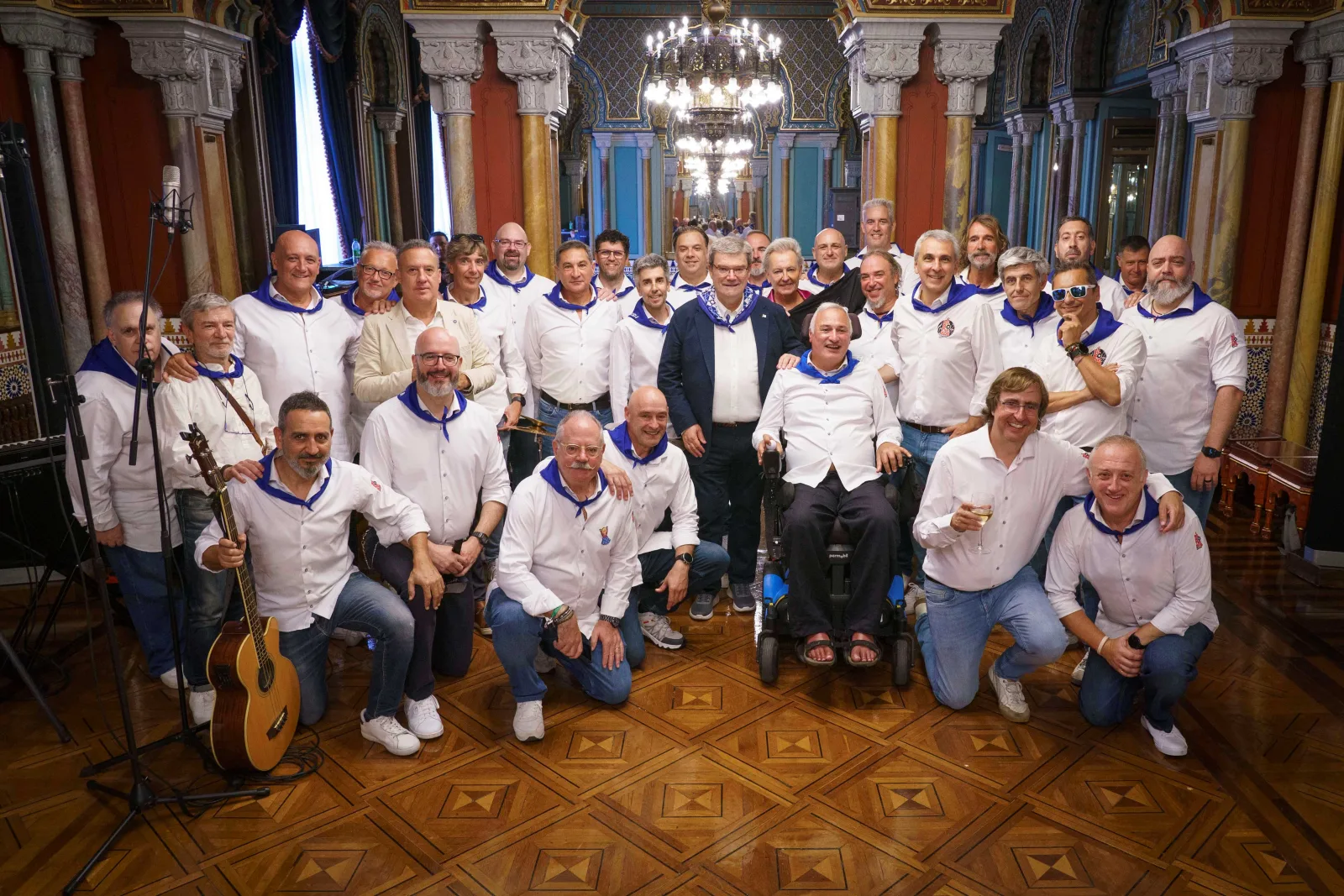 Foto de grupo de unas treinta personas con camisa blanca y pañuelo azul, con guitarras, junto al Alcalde en el salón del Ayuntamiento