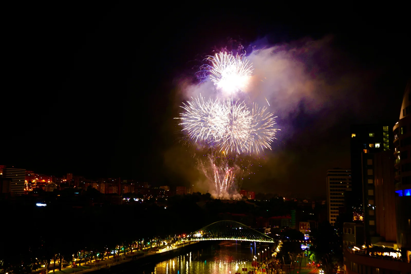 Fuegos artificiales sobre los edificios del centro de Bilbao, con la Ría iluminada