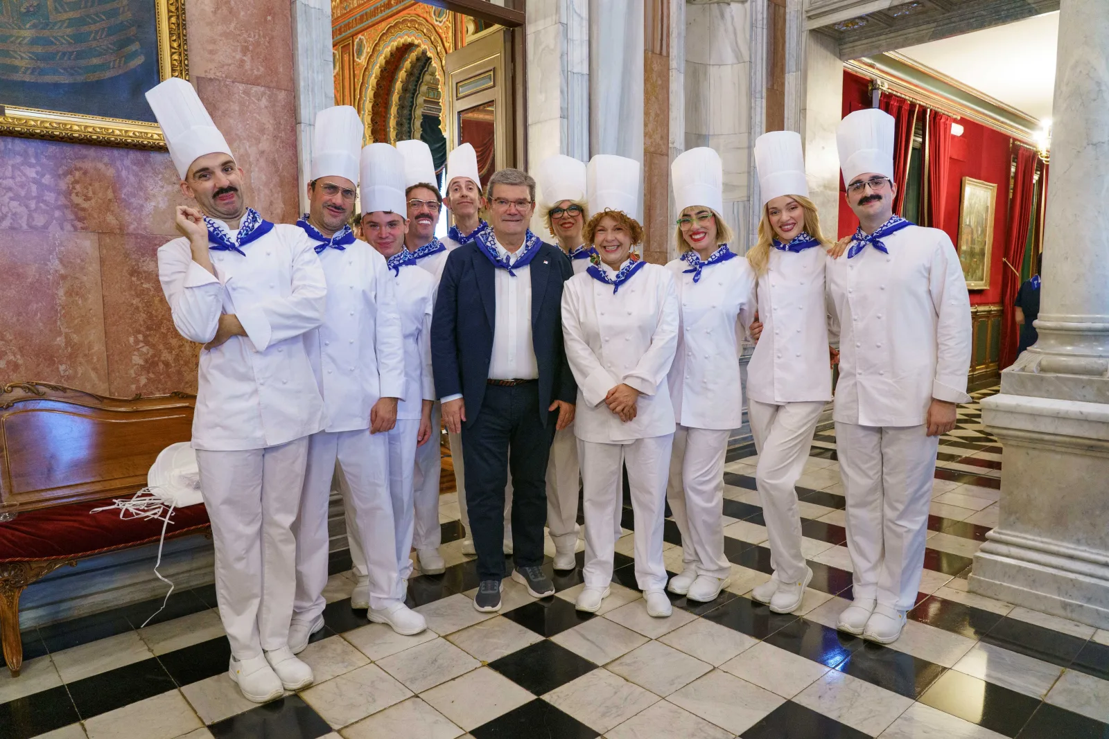 Un grupo con chaquetilla blanca y gorro alto de cocinero posa con el Alcalde en la escalera de mármol del Ayuntamiento