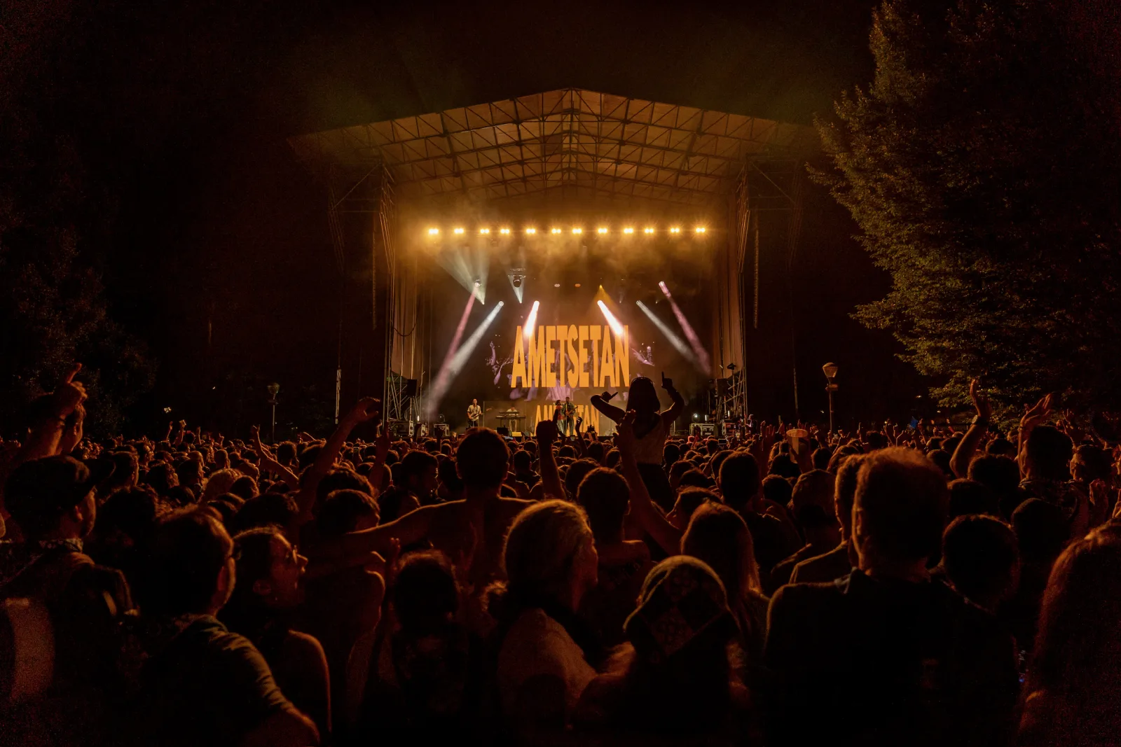 Vista desde el fondo del público hacia el escenario del Parque Europa, iluminado en tonos anaranjados, con la palabra AMETSETAN en la pantalla