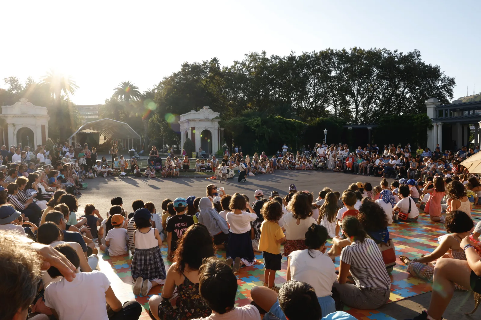 Público sentado en el césped de un parque durante un acto