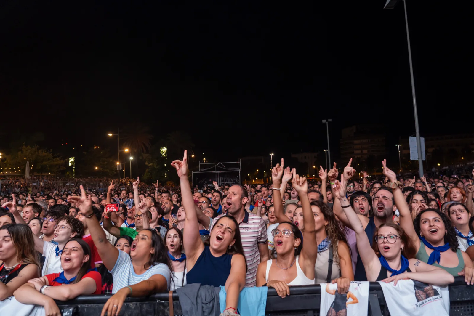 Primera fila del público cantando y con los brazos en alto contra la valla del escenario