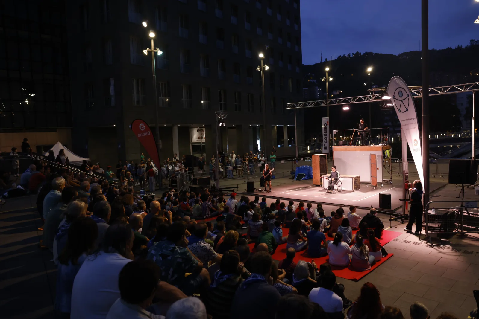 Público sentado ante un escenario de teatro de calle por la noche
