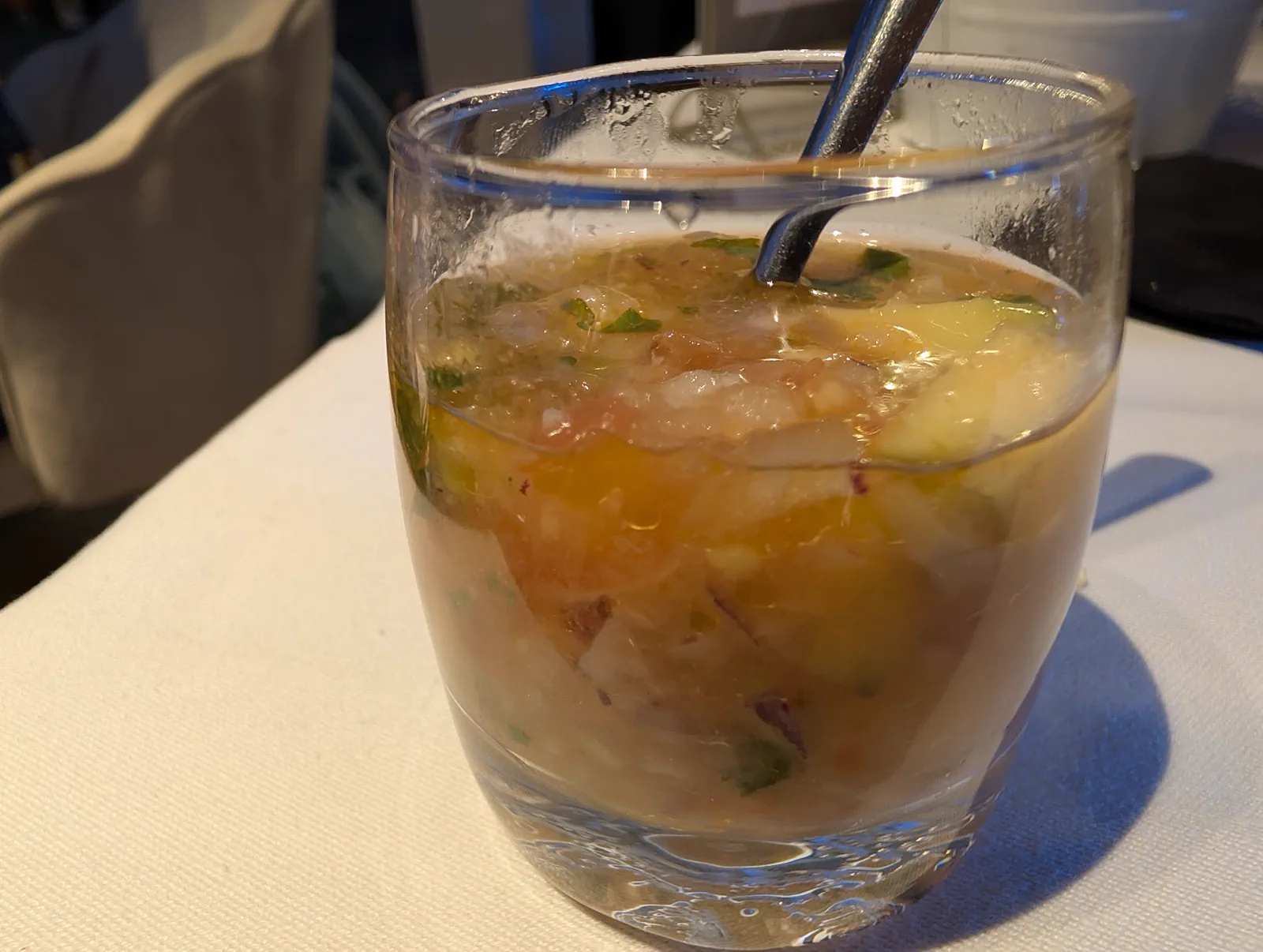 Vaso de ceviche de langostino, corvina y mango con cilantro y cebolla roja, con una cucharilla dentro