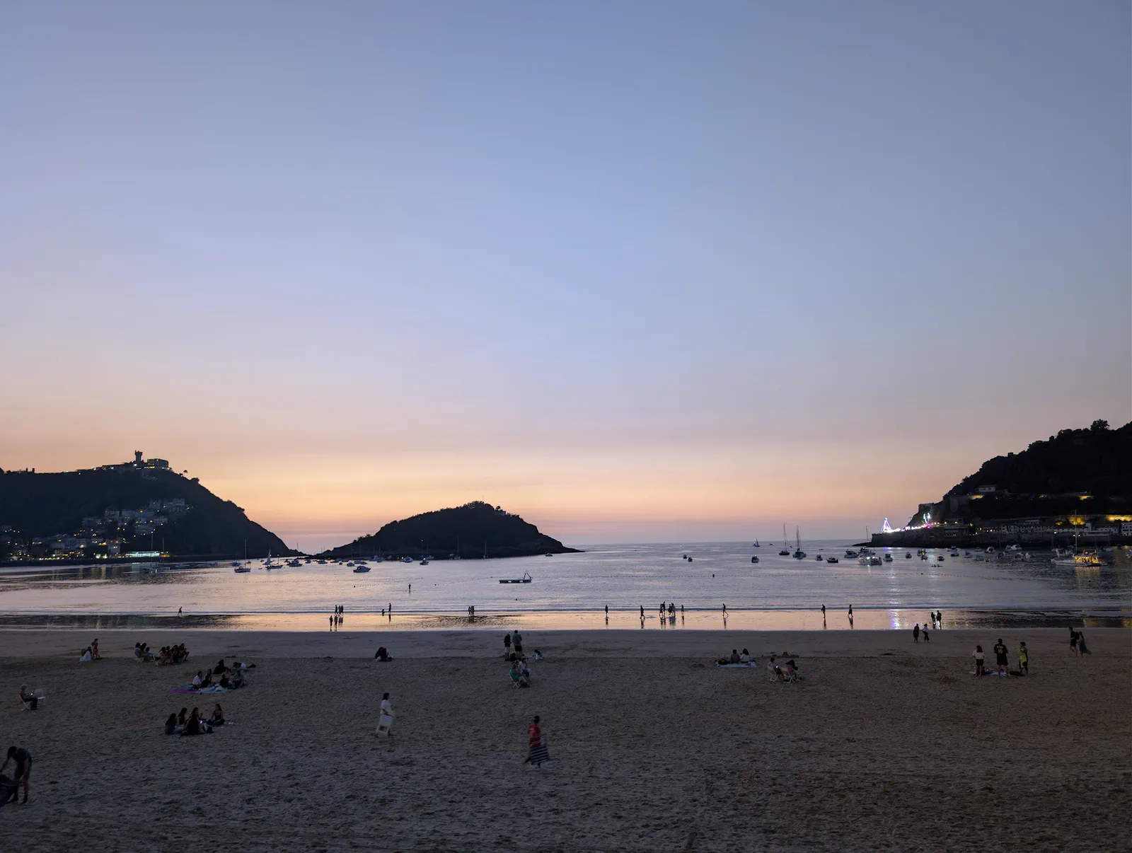 La bahía de la Concha con el cielo naranja tras la puesta de sol y las luces del ferial del Paseo Nuevo encendidas al pie del monte Urgull
