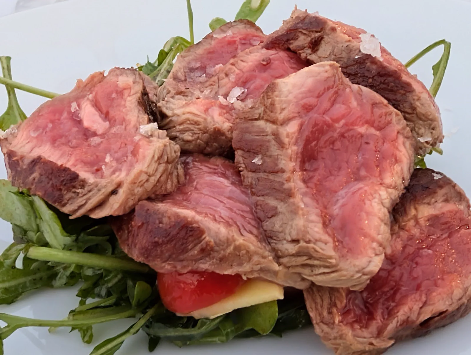 Lomo bajo de vaca de 24 meses laminado y con escamas de sal, sobre una base de rúcula con tomate y queso, el otro plato a elegir del menú