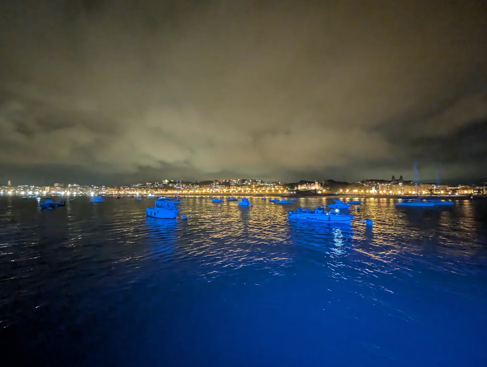 La bahía de la Concha de noche llena de embarcaciones fondeadas esperando los fuegos, con la playa y toda la fachada del paseo iluminadas al fondo