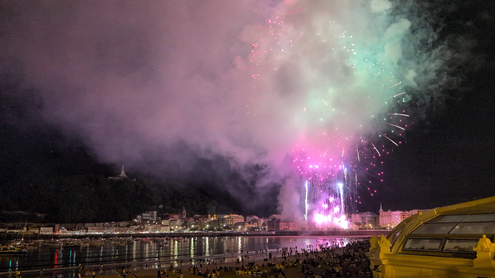 Fuegos artificiales rosas y verdes iluminando la nube de humo en la recta final de la tanda de Pirotecnia Tamarit