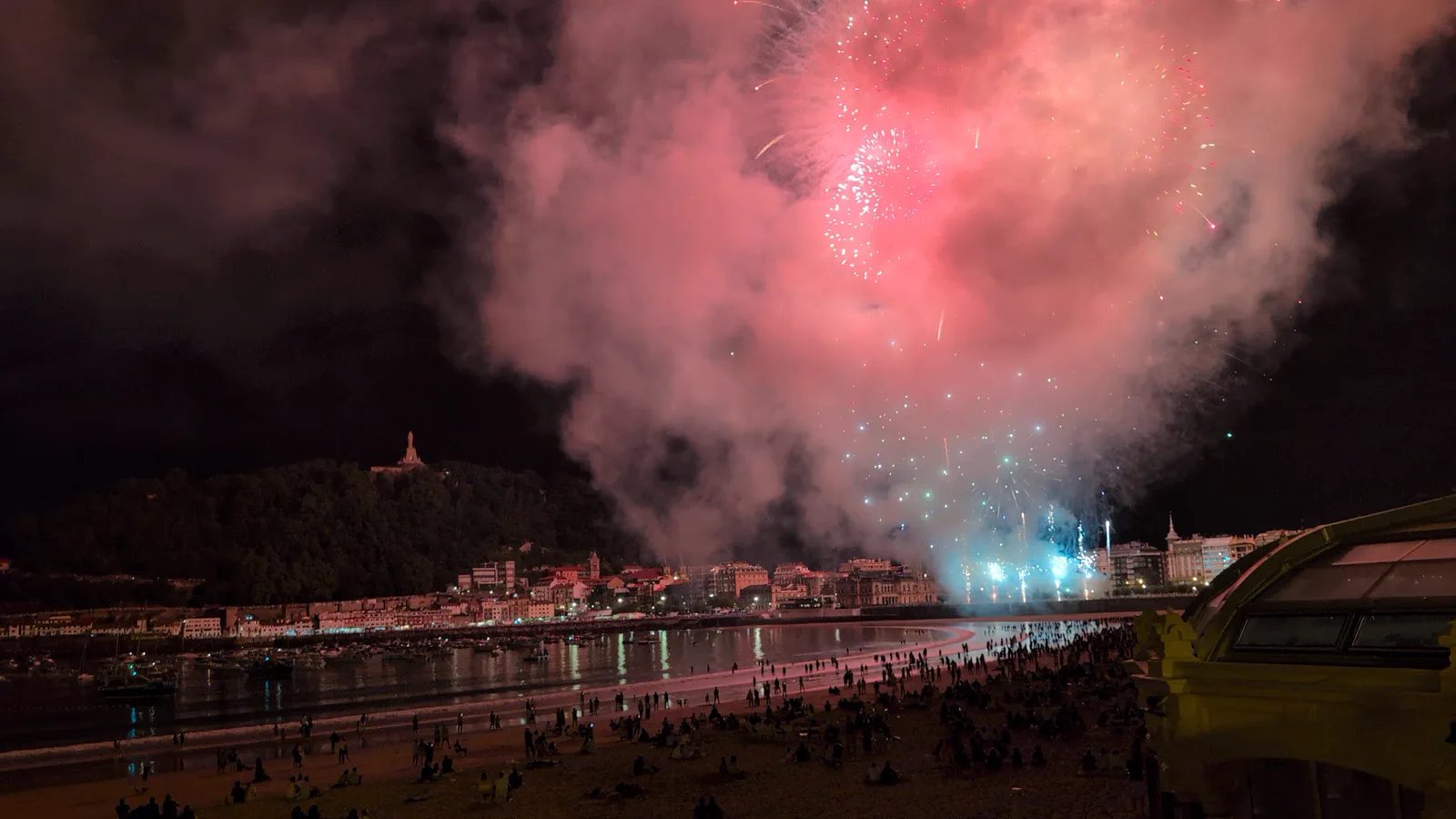 Estallido turquesa de la traca final de Pirotecnia Tamarit sobre la bahía de la Concha, con el humo teñido de rosa