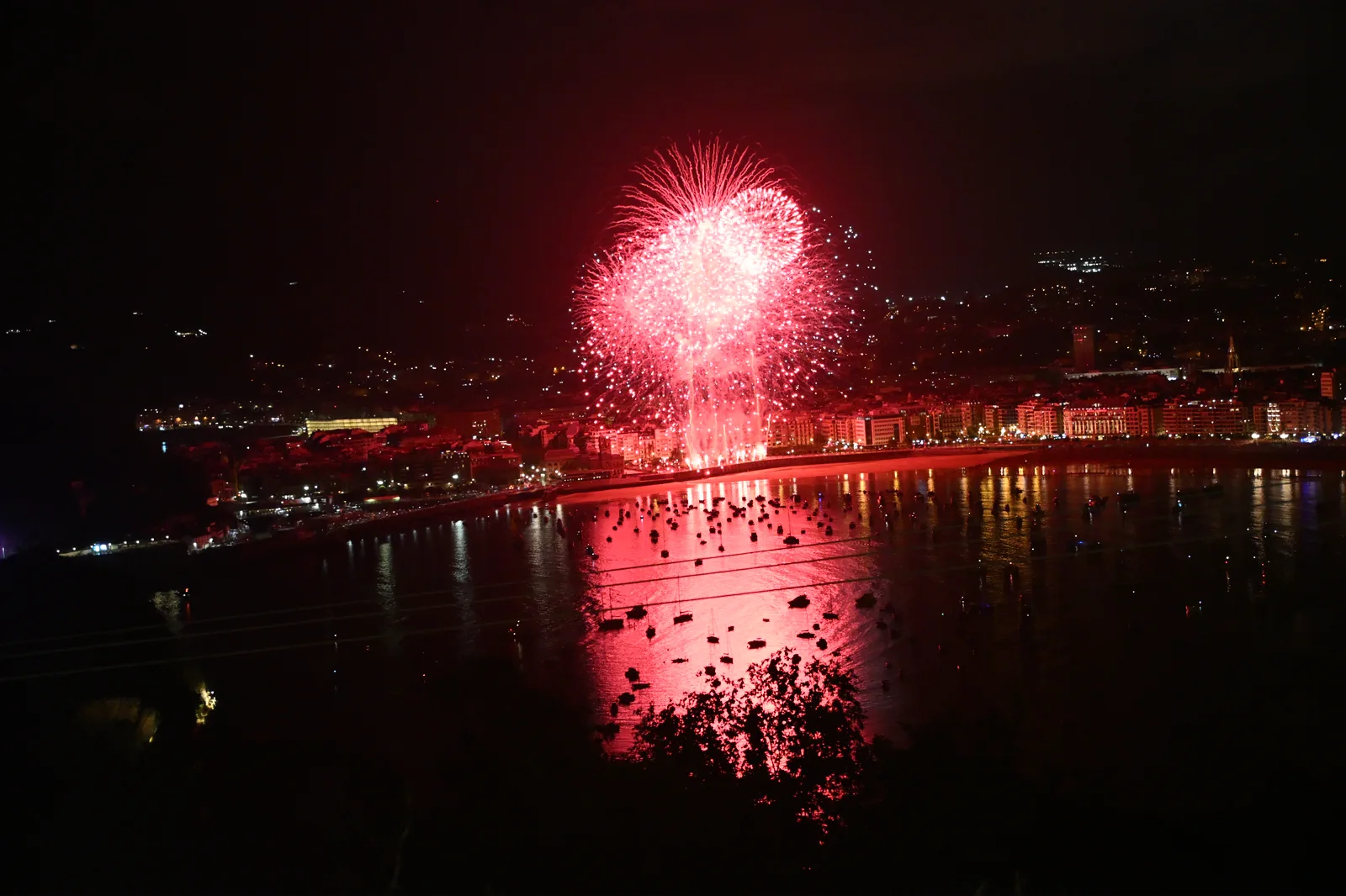 Fuegos artificiales rojos iluminando la bahía entera y el humo acumulado sobre el centro de la ciudad