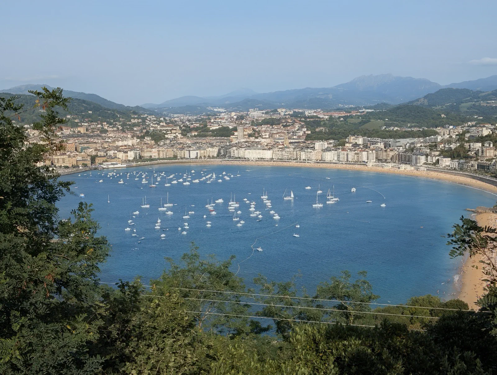 La bahía de la Concha completa vista desde el mirador del monte Igueldo a media tarde, con la playa, el puerto deportivo y las montañas al fondo