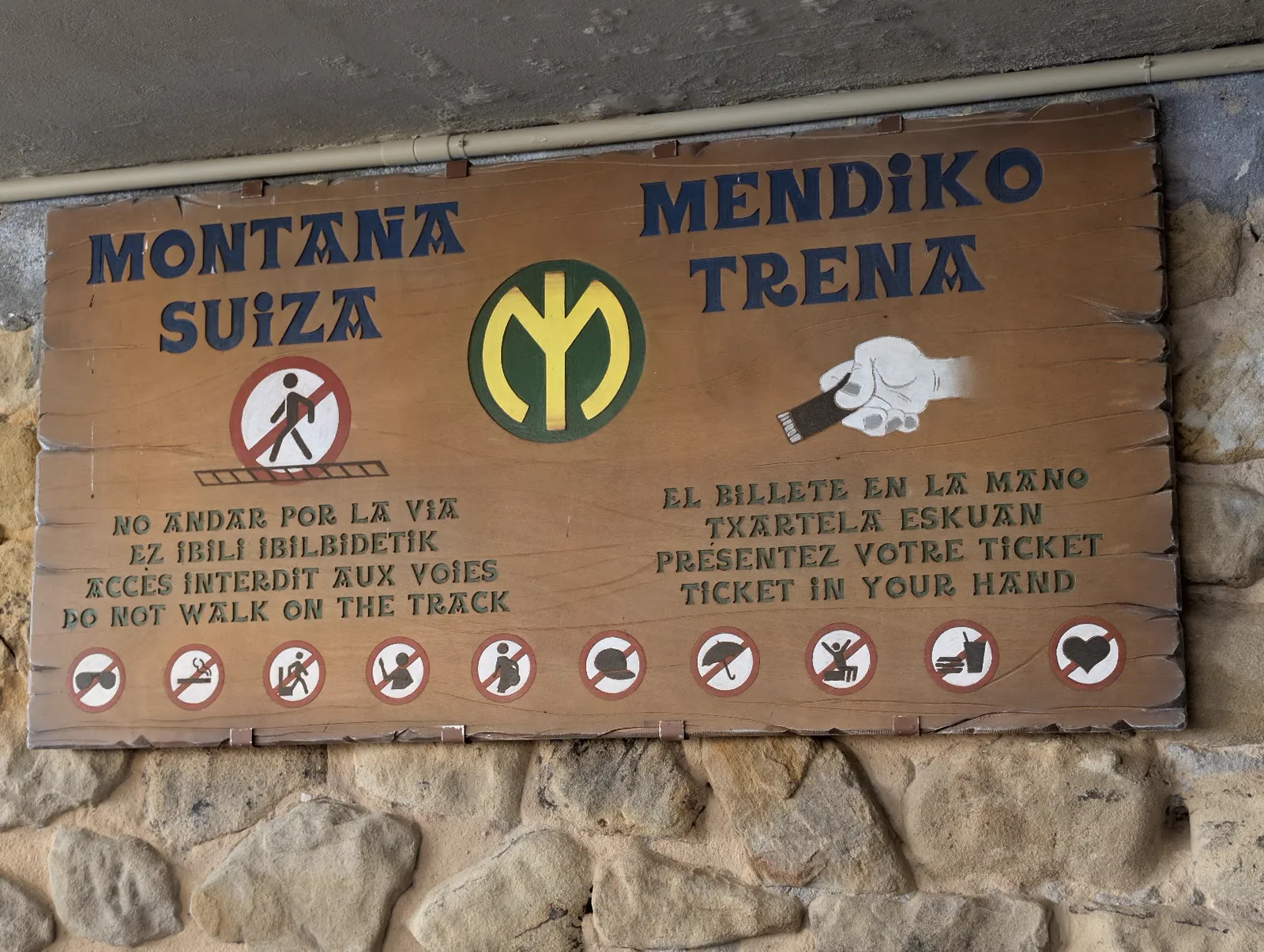 Cartel de madera pintado a mano de la atracción Montaña Suiza / Mendiko Trena, con los avisos en cuatro idiomas de no andar por la vía y llevar el billete en la mano