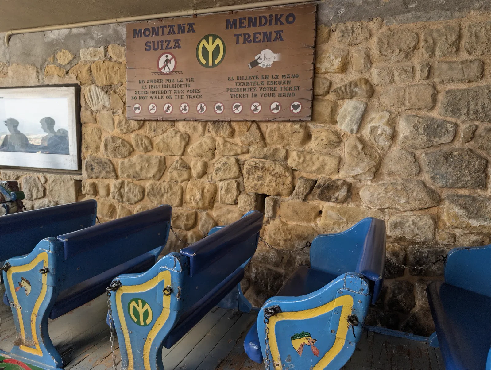 Interior de la estación de la Montaña Suiza del monte Igueldo, con los vagones de madera pintados de azul y amarillo alineados bajo el cartel de la atracción