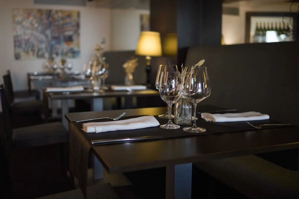 Comedor de Abakando con mesas vestidas de mantel oscuro, copas de vino y luz cálida de sobremesa