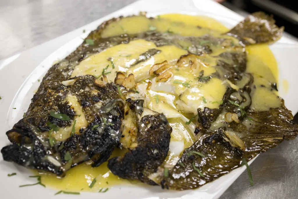 Rodaballo a la plancha con ajos laminados y refrito, servido en fuente blanca en Abakando