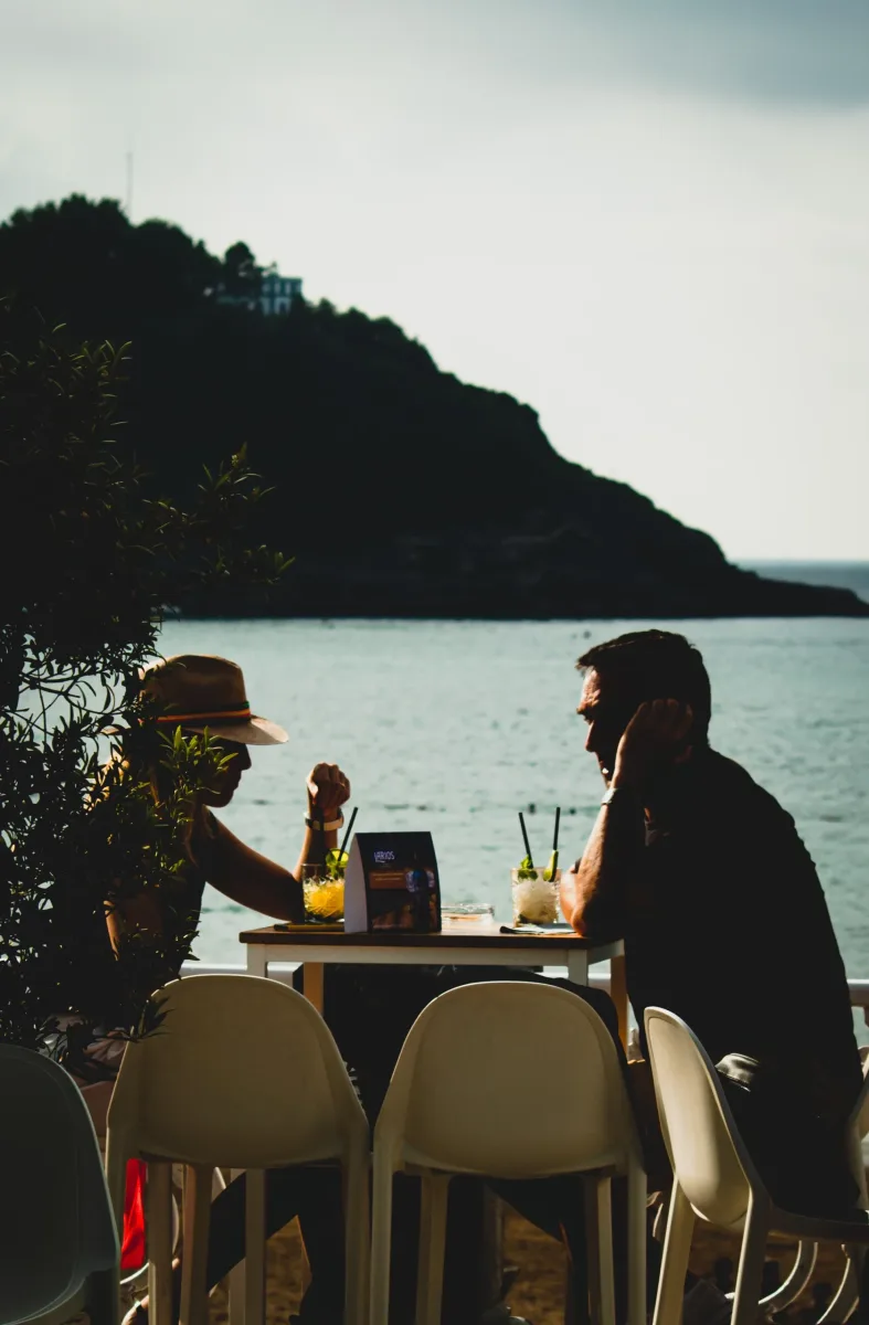 Dos personas tomando algo en la terraza del Bataplán al atardecer, con la bahía de la Concha y el monte Igueldo detrás