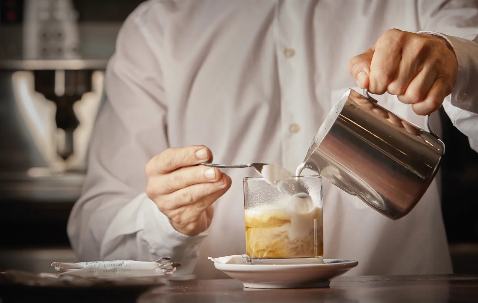 Un camarero de la cafetería de La Perla sirve la leche de un café detrás de la barra