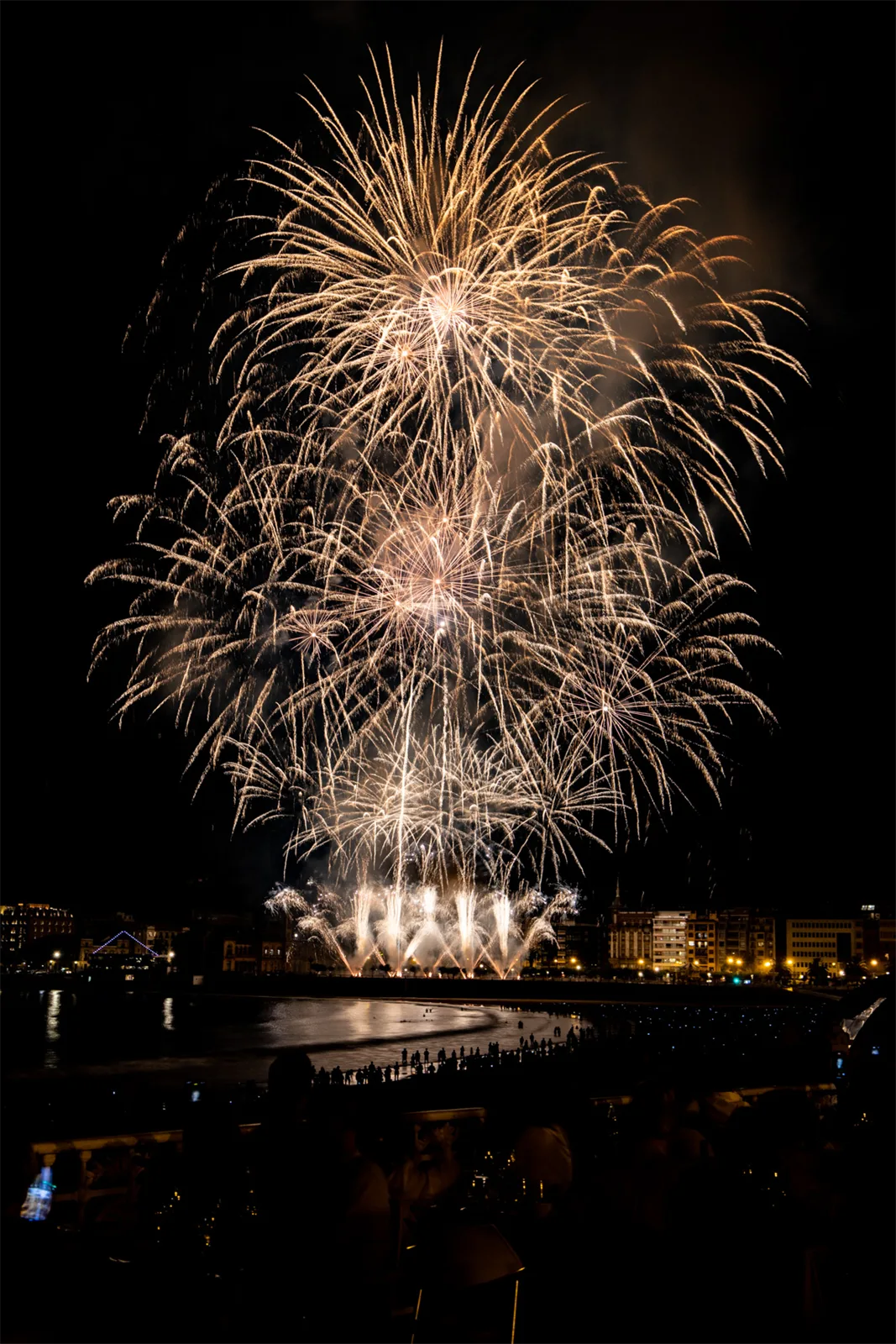 Fuegos artificiales de la Semana Grande estallando sobre la bahía de la Concha, vistos desde la terraza de La Perla, con clientes cenando en primer plano