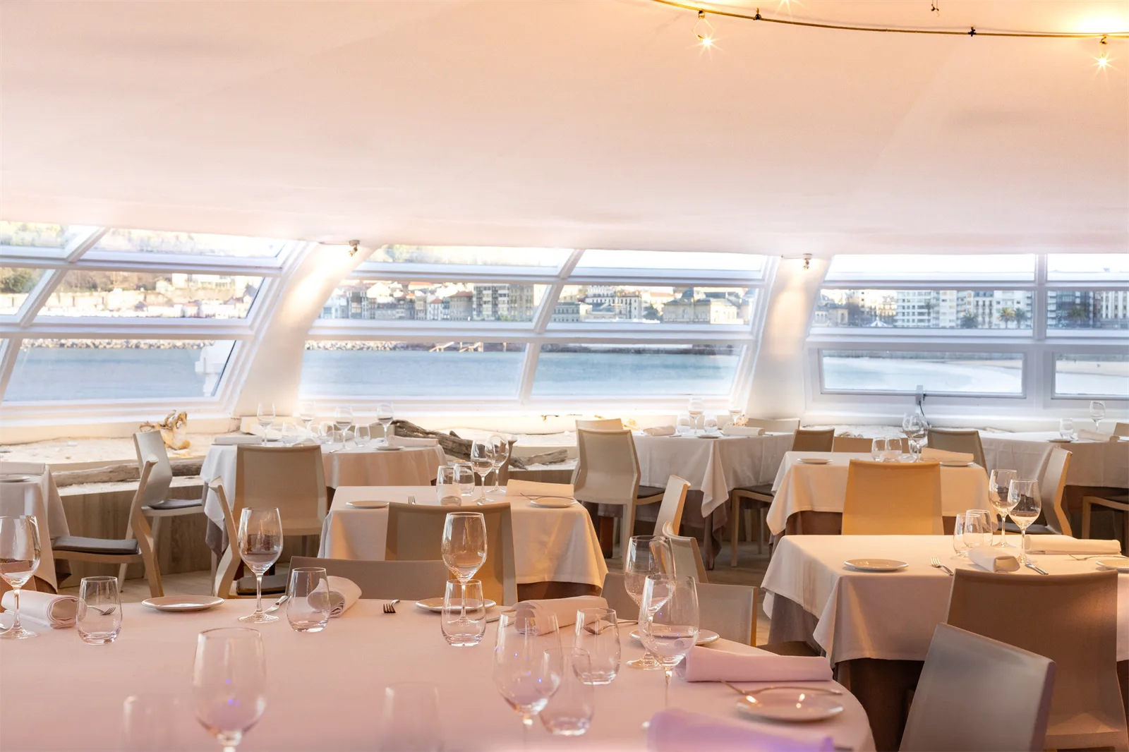 Comedor del Restaurante La Perla con las mesas preparadas y los ventanales asomados a la playa de la Concha