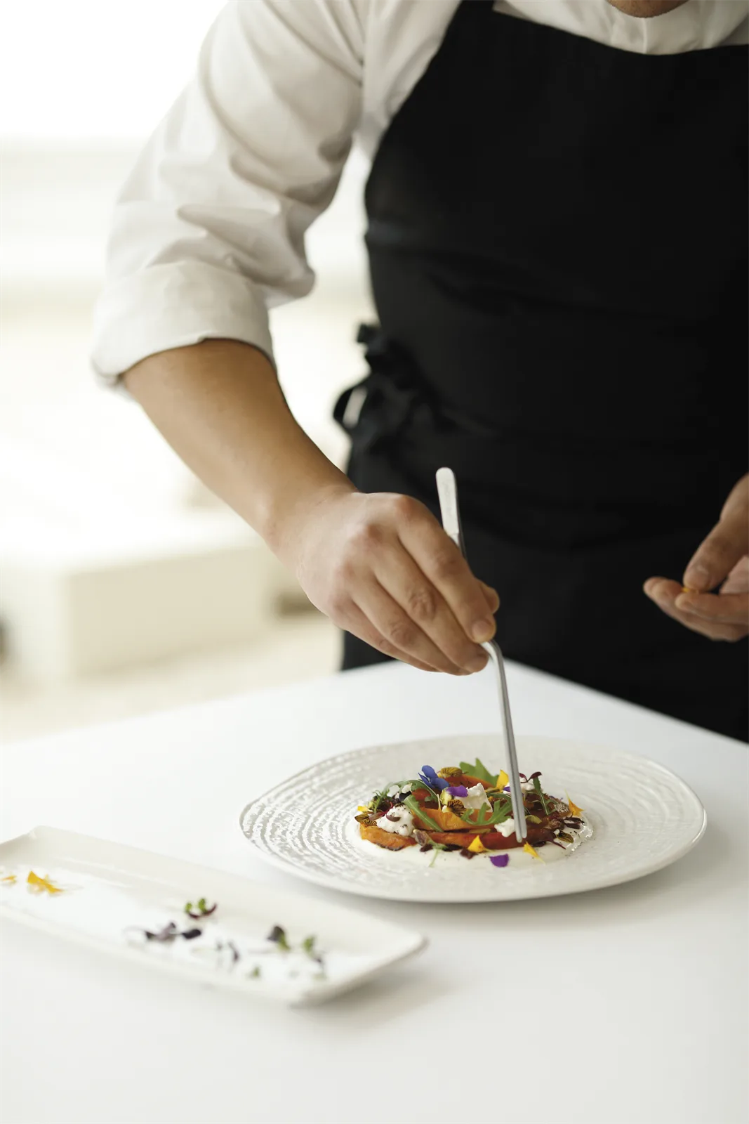 Un cocinero del Restaurante La Perla termina de emplatar un plato de temporada con flores comestibles