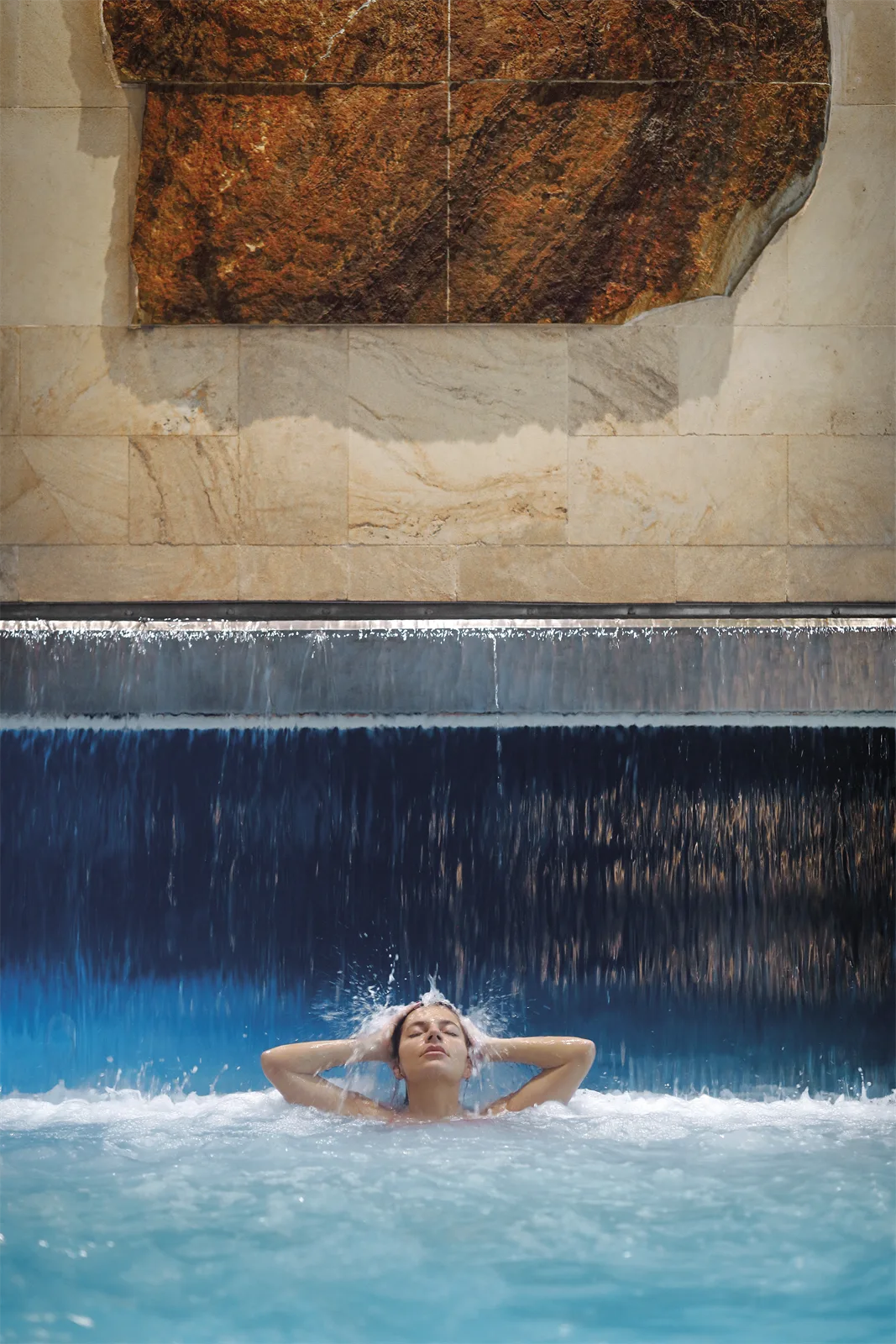 Una mujer se relaja bajo la cascada de agua de la piscina del talaso de La Perla