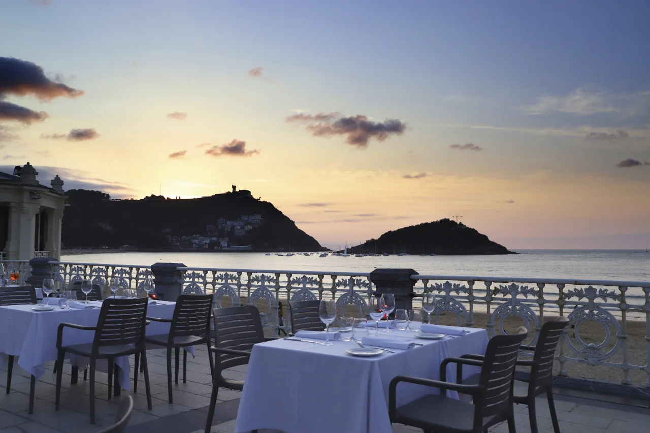 Terraza de La Perla, en el edificio de La Perla, al atardecer, con mesas puestas frente a la bahía de la Concha