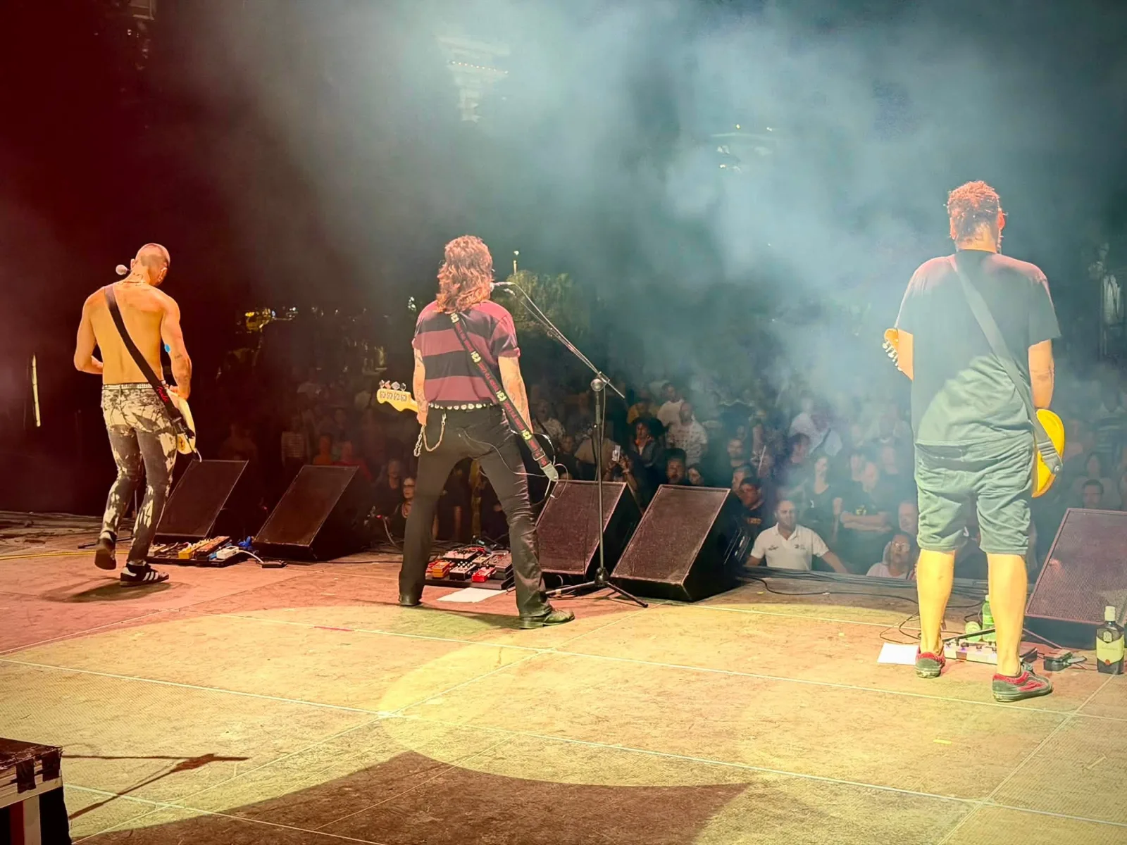 Tres músicos de espaldas, separados a lo ancho del escenario, tocan hacia un público que llena la primera fila tras las vallas