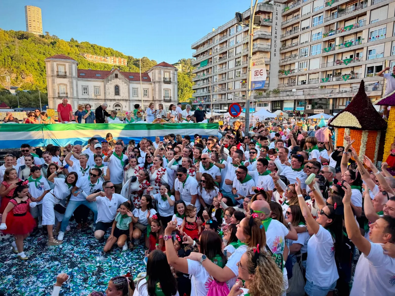 Centenares de personas de las distintas agrupaciones de carrocistas concentradas ante la tribuna al final del desfile, con el suelo cubierto de confeti