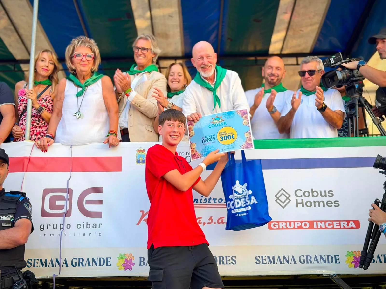 Joven con polo rojo sostiene ante la tribuna un diploma en el que se lee «Anchoas Codesa — Premio Internacional 300 €» junto a una bolsa de tela del mismo patrocinador