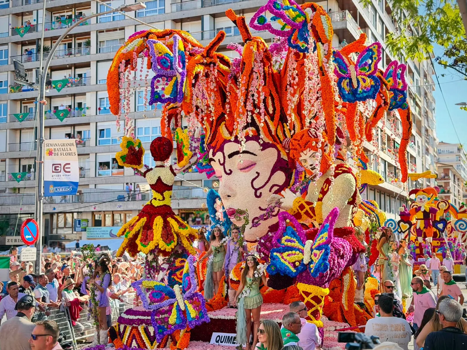 La carroza «Quimera», con un rostro monumental de melena anaranjada y grandes mariposas de flor, y varias personas disfrazadas de criaturas del bosque sobre la plataforma