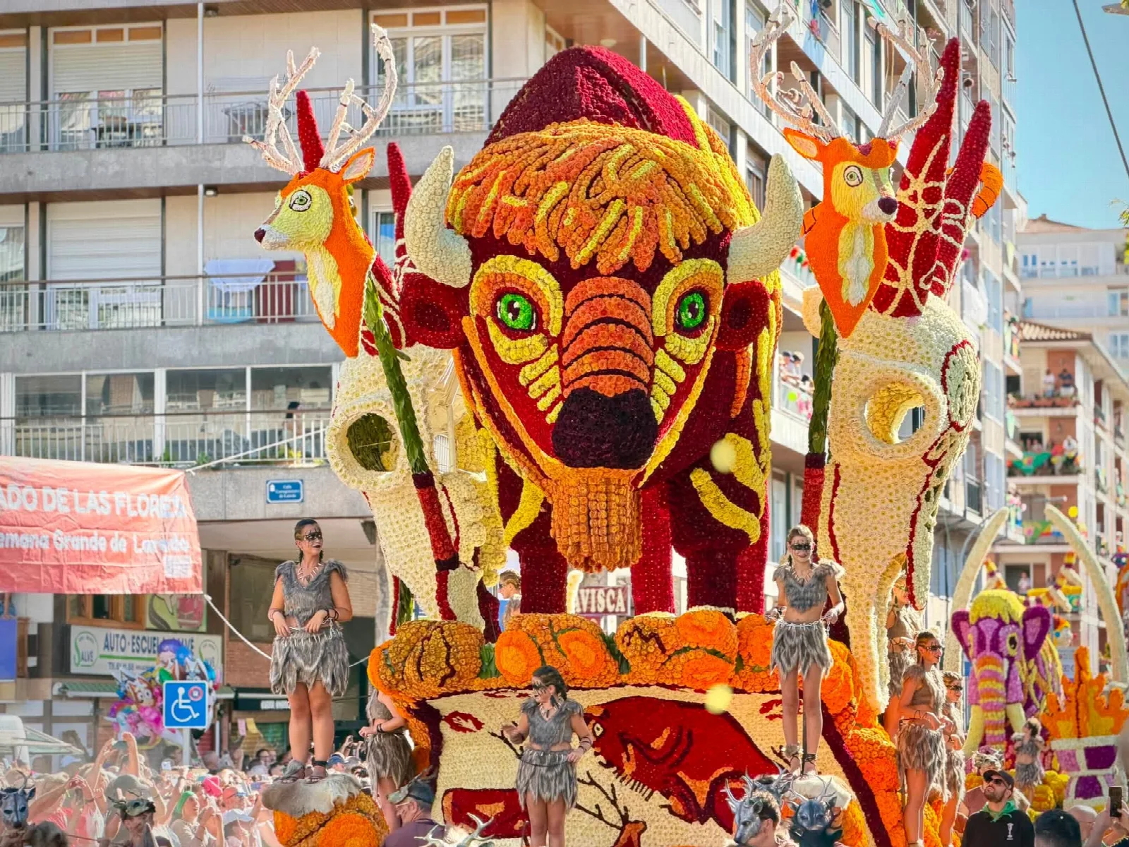La carroza «Soñando Altamira», con un bisonte monumental de flor roja y amarilla flanqueado por dos ciervos, y personas vestidas con pieles sobre la plataforma