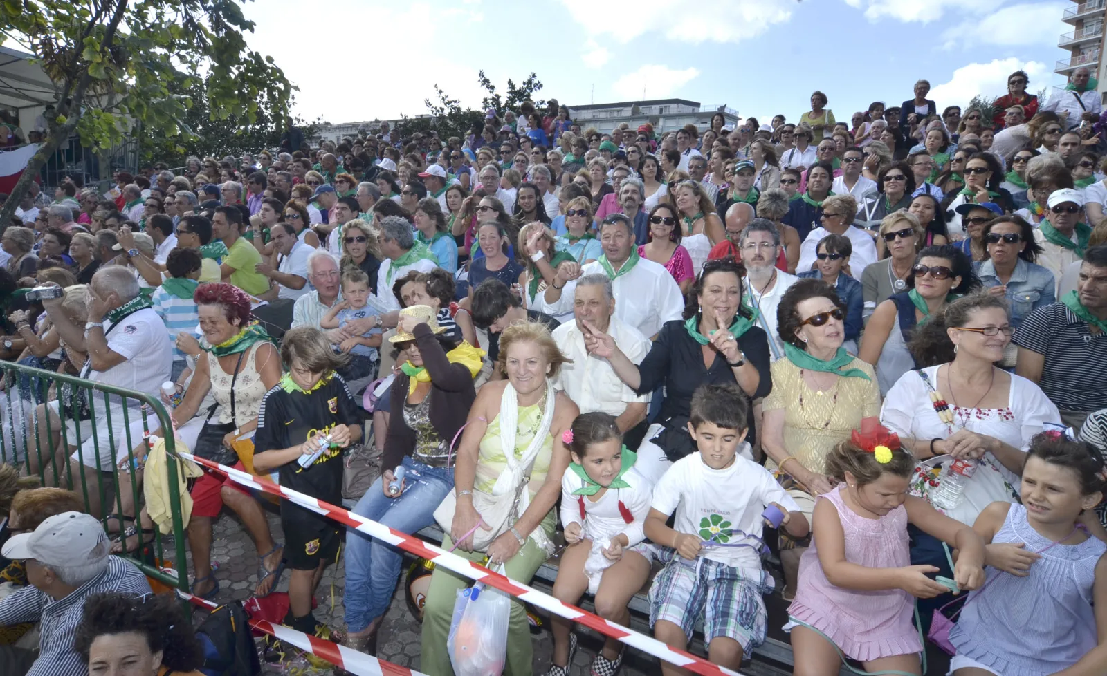 Gradas abarrotadas de público con pañuelo verde al cuello esperando el paso de las carrozas
